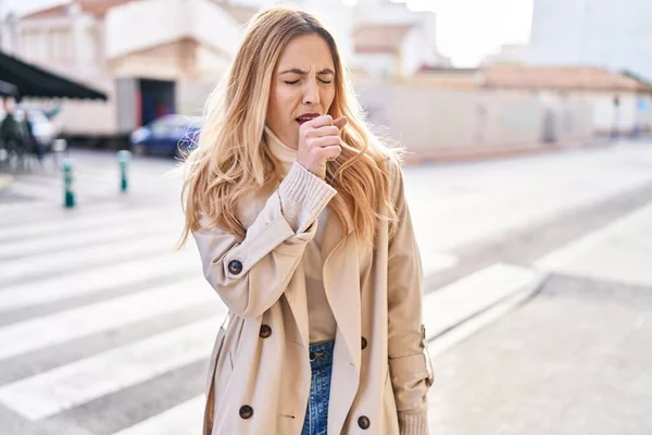 Young blonde woman coughing at street