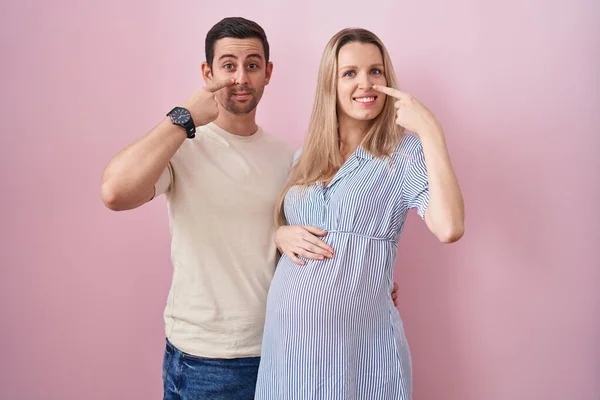 Casal Jovem Esperando Bebê Sobre Fundo Rosa Apontando Com Mão — Fotografia de Stock