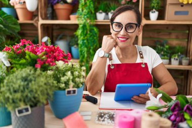 Young beautiful hispanic woman florist smiling confident using touchpad at flower shop