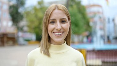 Parkta kendinden emin gülümseyen genç sarışın kadın.