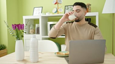 Genç Arap adam evde kahvaltı yaparken dizüstü bilgisayar kullanıyor.