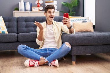 Genç İspanyol adam akıllı telefonuyla başarıyı kutluyor mutlu bir gülümsemeyle ve kazanan yüz ifadesiyle elini kaldırarak. 