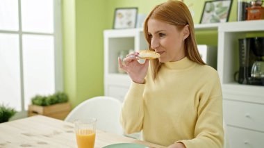 Young blonde woman using laptop having breakfast at home