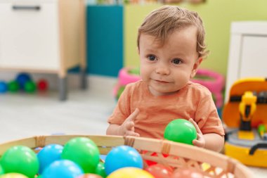 Anaokulunda yerde taşaklarıyla oynayan sevimli sarışın çocuk.