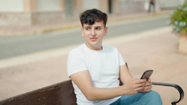 Non binary man using smartphone sitting on bench at park