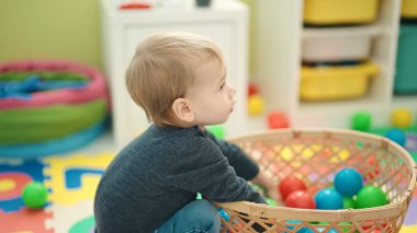 Anaokulunda yerde taşaklarıyla oynayan sevimli sarışın çocuk.