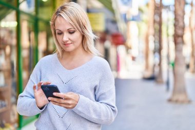 Sokakta akıllı telefon kullanan, kendine güvenen genç sarışın kadın.