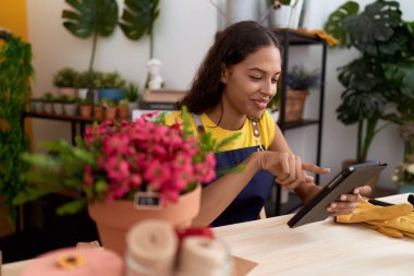 Young african american woman florist smiling confident using touchpad at flower shop