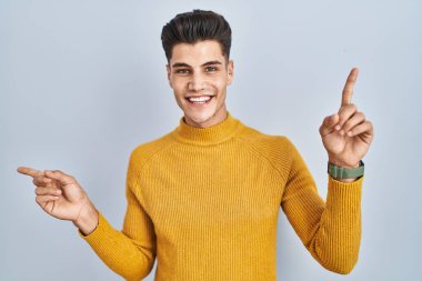 Mavi arka planda duran genç İspanyol adam parmaklarıyla farklı yönleri gösteren kendine güvenle gülümsüyor. reklam için kopyalama alanı 