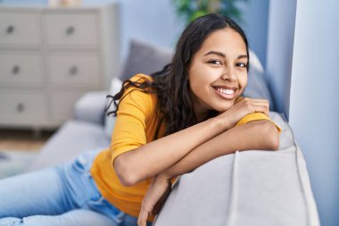 Afro-Amerikalı genç bir kadın. Evdeki koltukta kendinden emin bir şekilde oturuyor.