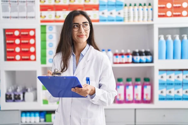Young Hispanic Girl Pharmacist Writing Report Clipboard Pharmacy — Stock fotografie