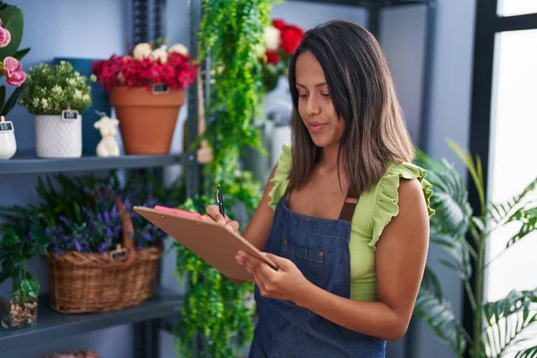 Young Hispanic Woman Florist Writing Document Organize Shelving Florist Store — Stockfoto