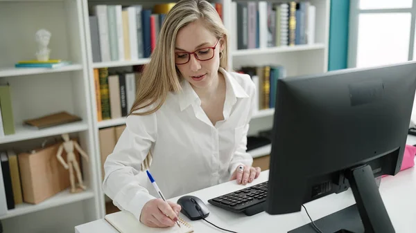 図書館大学でノートにコンピュータライティングを使用して若いブロンドの女性学生 — ストック写真