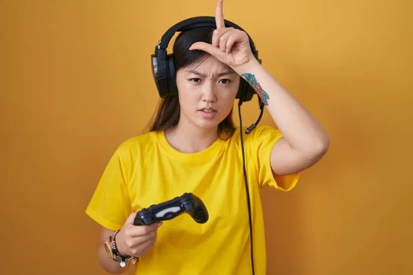 中国年轻女子玩电子游戏时牵着控制器 用手指在额头上取笑那些做失败者动作的人 嘲笑和侮辱 — 图库照片