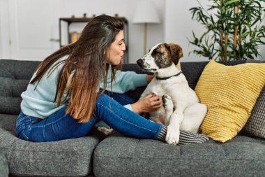 Genç bir kadın evdeki kanepede oturan köpeğe sarılıyor.