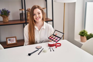 Young caucasian woman holding blush palette looking positive and happy standing and smiling with a confident smile showing teeth 