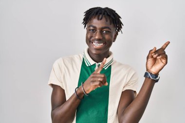 Afrikalı bir adam izole edilmiş arka planda duruyor gülümsüyor ve kameraya bakıyor iki eliyle ve parmaklarıyla yandan işaret ediyor.. 