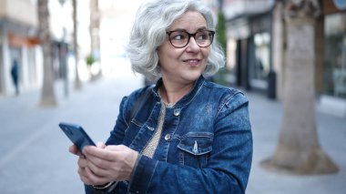 Middle age woman with grey hair using smartphone at street