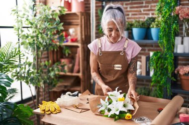 Orta yaşlı, kır saçlı kadın çiçekçi çiçekçide çiçek buketi yapıyor.