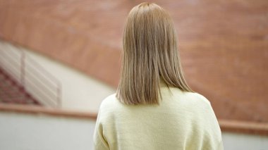 Young blonde woman standing backwards at street