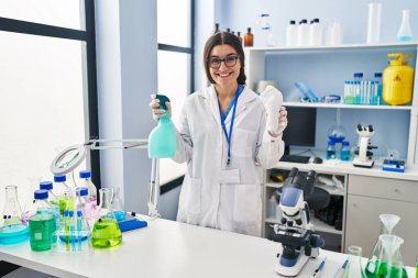 Young hispanic woman wearing scientist uniform cleaning using sanitizer gel at laboratory