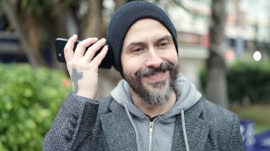 Genç kel adam gülümsüyor. Parktaki akıllı telefondan kendine güvenen sesli mesaj dinliyor.