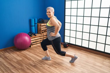 Middle age woman smiling confident stretching leg at sport center