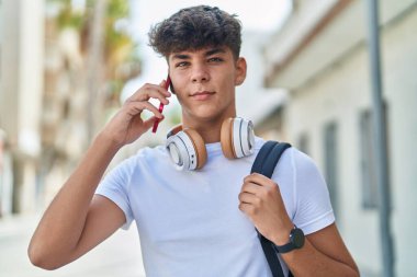 Young hispanic teenager student talking on smartphone with relaxed expression at street