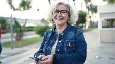 Middle age woman with grey hair using smartphone at street