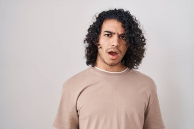 Beyaz arka planı üzerinde duran kıvırcık saçlı İspanyol bir adam. Şok olmuş yüzü, şüpheci ve alaycı görünüyor. 