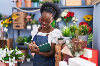 African american woman florist smiling confident writing on notebook at florist store