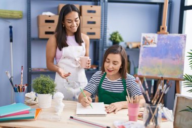 Two women artists drinking coffee drawing on notebook at art studio