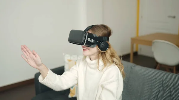 年轻的金发女人在家里用虚拟现实眼镜玩电子游戏 — 图库照片
