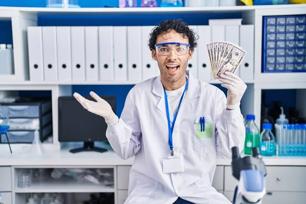 科学研究所で働くヒスパニック系男性幸せな笑顔で達成を祝うお金を保持し 手を上げと勝者の式 — ストック写真