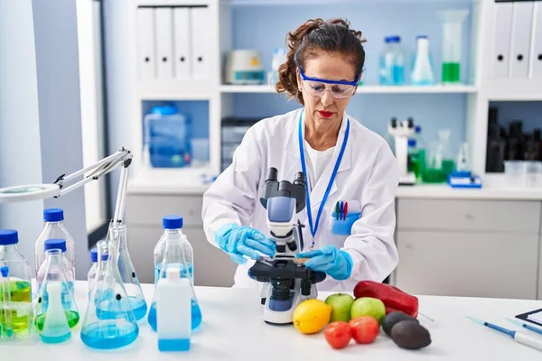 Middle age hispanic woman looking through microscope at laboratory