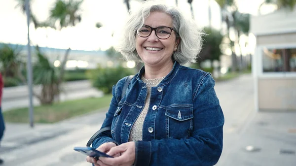 Middle age woman with grey hair using smartphone at street