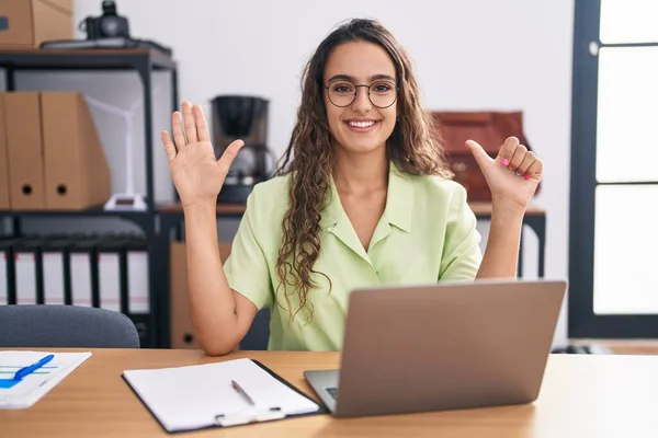 stock image Young hispanic woman working at the office wearing glasses showing and pointing up with fingers number six while smiling confident and happy. 