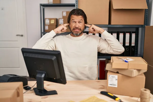 Handsome middle age man working at small business ecommerce covering ears with fingers with annoyed expression for the noise of loud music. deaf concept.