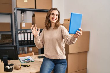 Ecommerce 'de çalışan genç bir kadın tabletle video çekiyor. Pozitif ve mutlu görünüyor. Kendine güvenen bir gülümsemeyle dişlerini gösteriyor. 