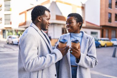 Kadın ve erkek sokakta kahve içerken yan yana duruyorlar.