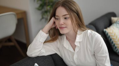 Sarışın genç bir kadın evdeki koltukta kendinden emin bir şekilde oturarak gülümsüyor.