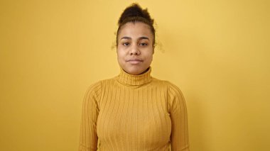 Young african american woman standing with serious expression over isolated yellow background