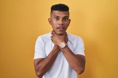 Young hispanic man standing over yellow background shouting suffocate because painful strangle. health problem. asphyxiate and suicide concept. 