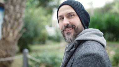 Genç kel adam parkta kendine güvenerek gülümsüyor.