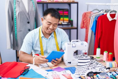 Genç Çinli terzi terzide dokunmatik ped kullanarak gülümsüyor.