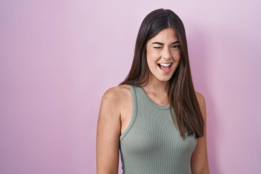 İspanyol kadın pembe arka planda durmuş kameraya seksi bir ifadeyle bakıyor, neşeli ve mutlu bir yüzle.. 