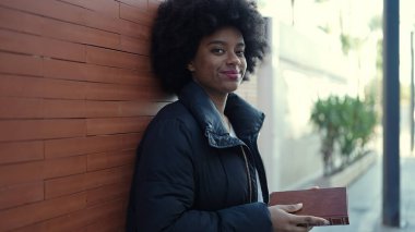 African american woman reading book leaning on wall at street