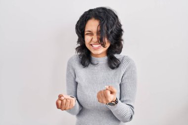 Koyu renk saçlı İspanyol kadın izole edilmiş arka planda mutlu ve heyecanlı bir şekilde kollarını kaldırıp, gülümseyip, başarı çığlıkları atarak zafer jesti yapıyor. kutlama konsepti. 