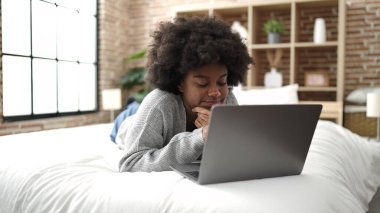 African american woman using laptop lying on bed at bedroom