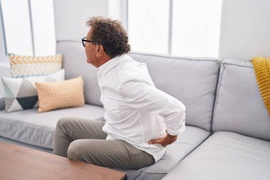 Middle age man suffering for backache sitting on sofa at home